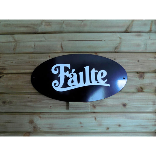 Black oval metal sign with white 3D “Fáilte” text and pre-drilled holes for hanging.