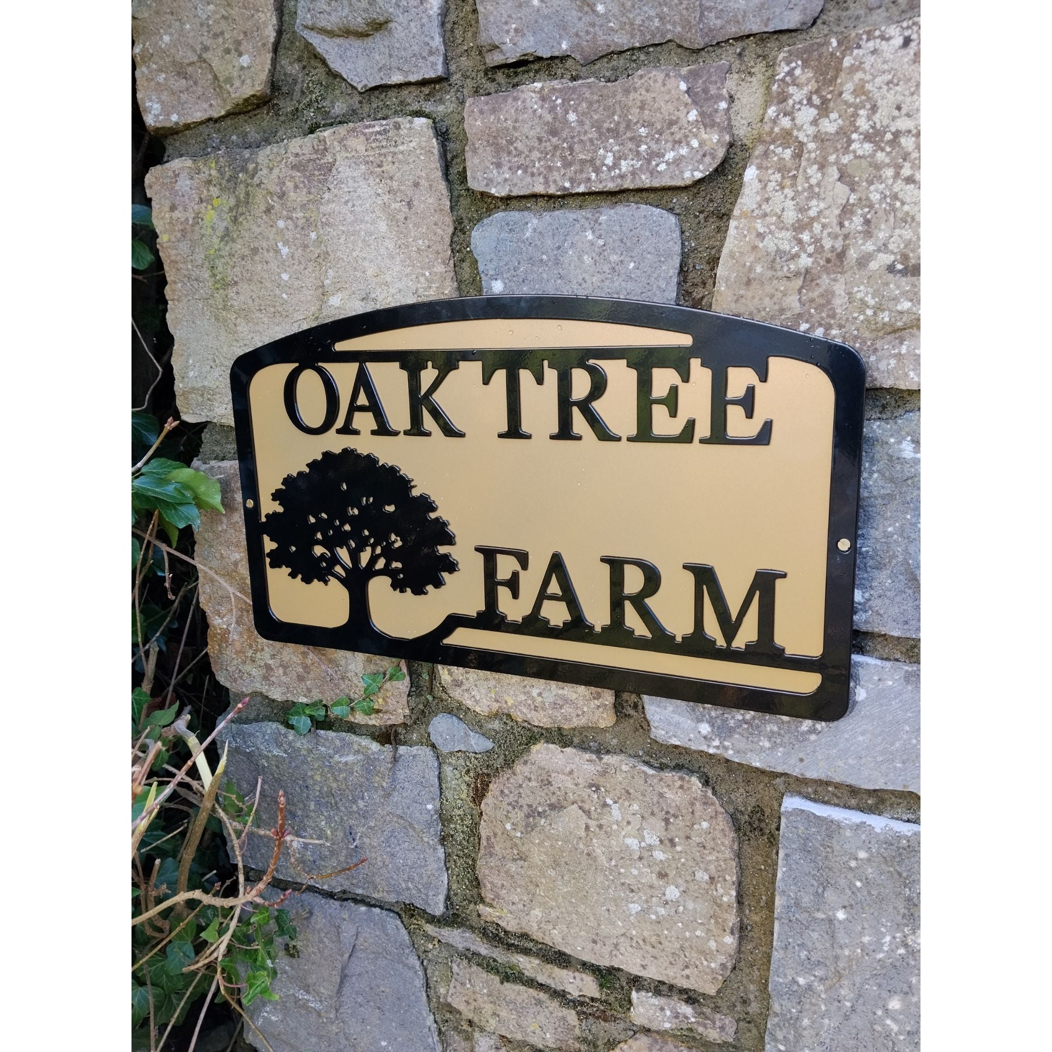 custom metal sign with black text 'oak tree farm' and tree design on gold backing plate hanging on a customer pillar