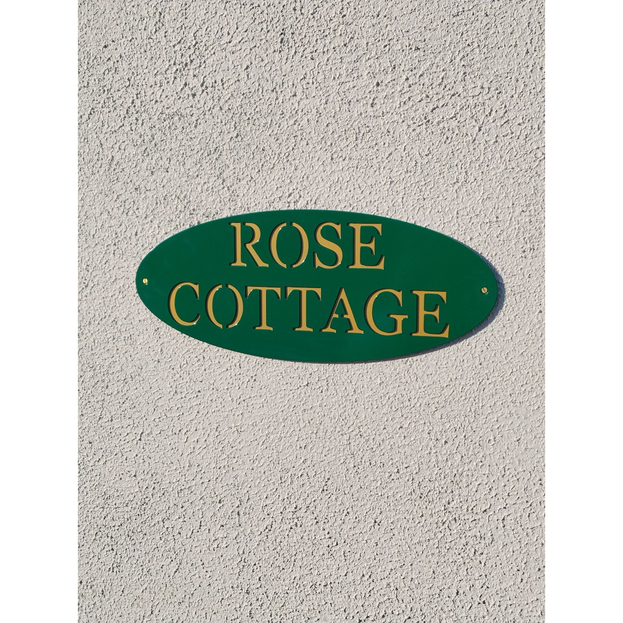 Oval custom metal sign in emerald green with gold text 'Rose Cottage' on gold backing plate, hanging on customer wall in waterford, ireland