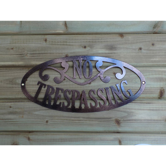 Oval two toned black and bronze metal sign with the words “No trespassing” mounted on a wooden background