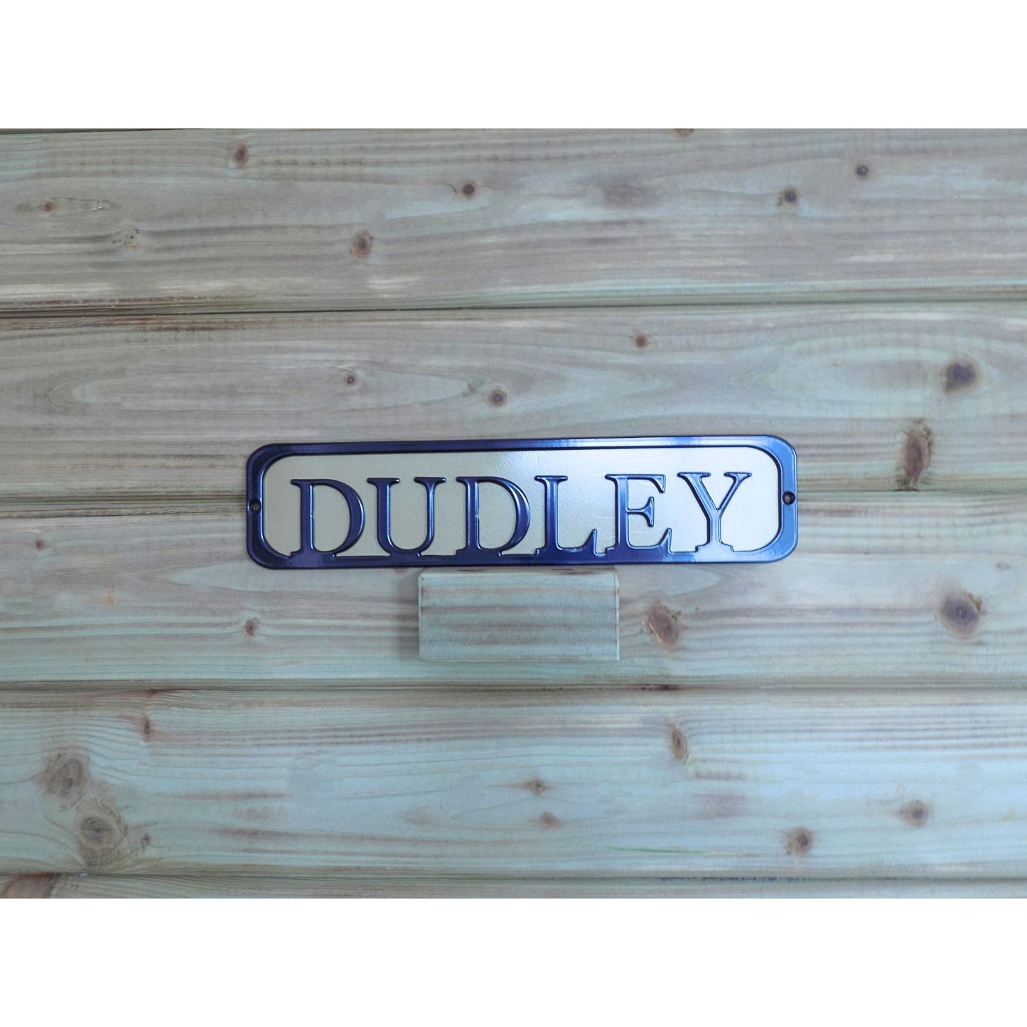 Metal sign with text 'DUDLEY' black on a Gold backing plate