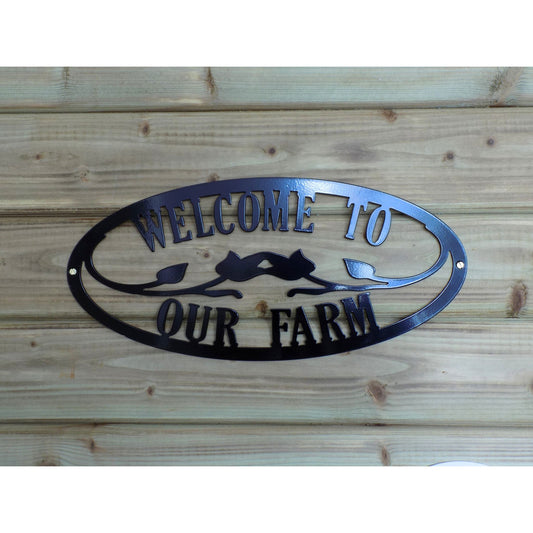 Black oval metal sign with cutout text “Welcome to Our Farm” and decorative leaves, mounted on wood. Powder-coated and handmade in Ireland.